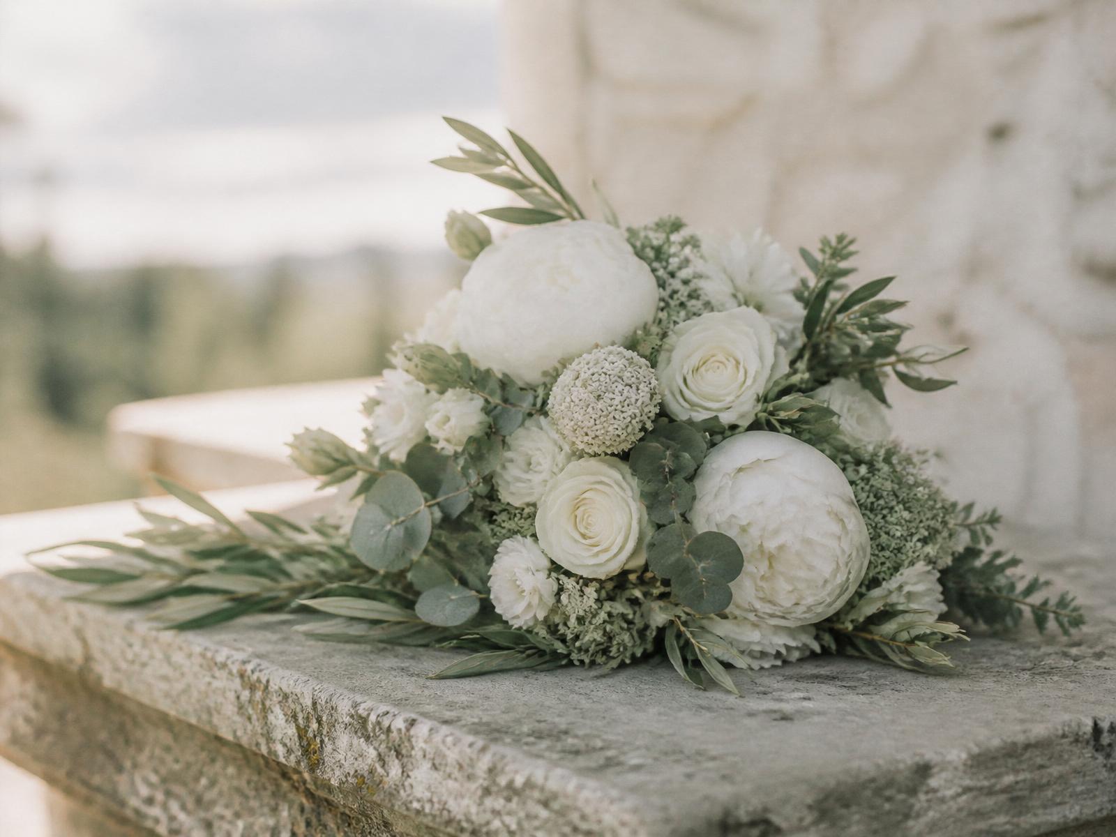 White peony and olive branch sympathy arrangement resting on pale stone
